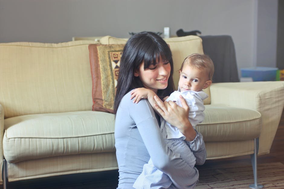 A mother lovingly embraces her baby indoors on a comfortable sofa capturing warmth and togetherness.